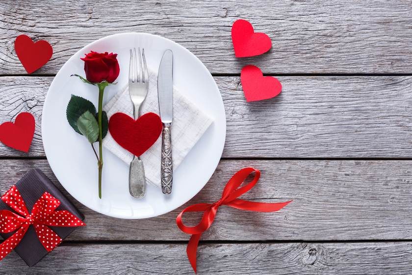 Romantic dinner concept. Valentine day or proposal background. Top view of restaurant wooden table with heart and rose with cutlery on plate. Copy space on rustic wood
