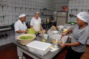 Auxiliar de cozinha e cozinheiras preparando almoço