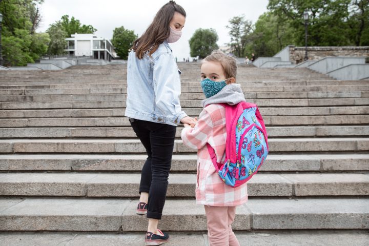 Little girl schoolgirl in a mask holds her mother's hand and goes to school.
